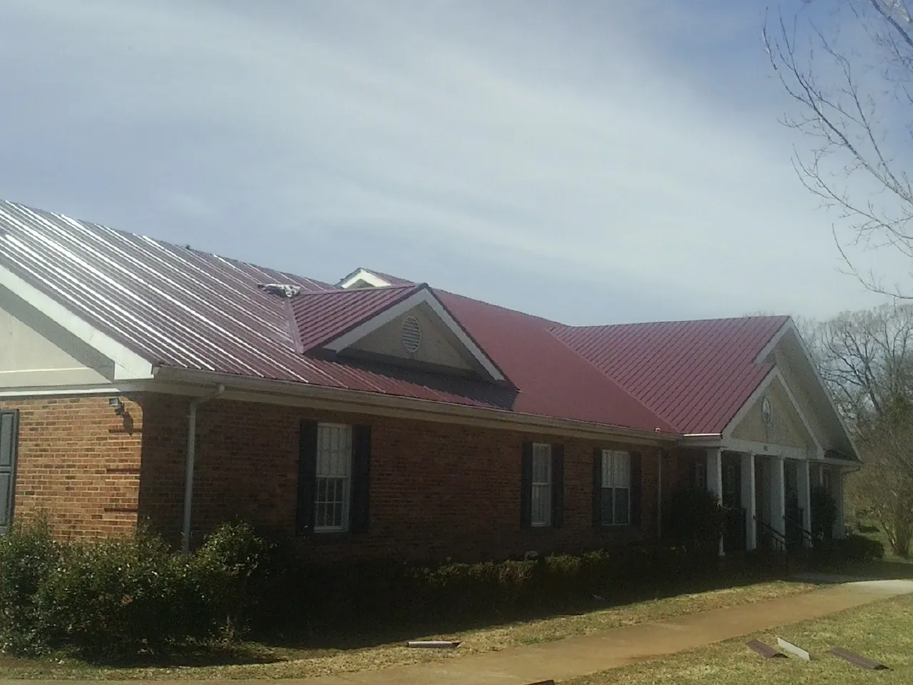 Red metal roof with gabled entries on a long brick building, from a Hail Damage Roof Repair job in Citra