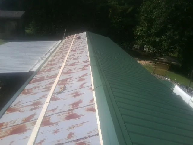 Old rusted panels beside newly installed green metal roofing — Wind Damage Roof Repair by Roofing Brothers in Citra