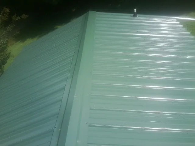New green metal panels meeting at the ridge of a roof — Flat Roof Repair work by our crew in Citra