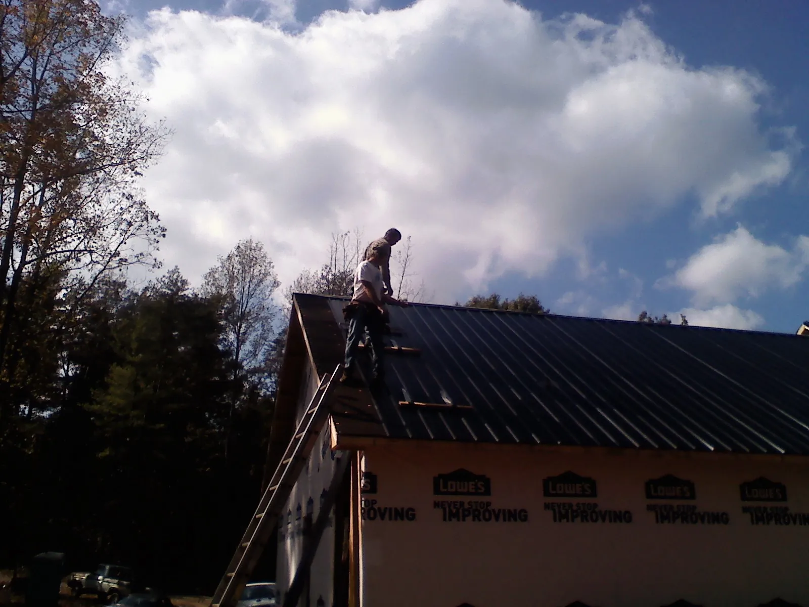 Roofer fastening dark metal panels high against a cloudy sky, from a Roof Inspection job in Citra